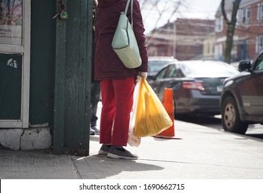 New York, NY / USA - February 28, 2020: Asian Woman Stands Outside A Corner Store Waiting With Plastic Bag In Hand