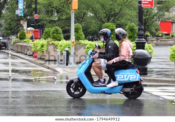 New York, NY / USA - July 24, 2020: Couple\
Rides Revel Motor Scooter in Rain Lower Manhattan in New York City\
During Covid-19 Pandemic Phase 4,\
