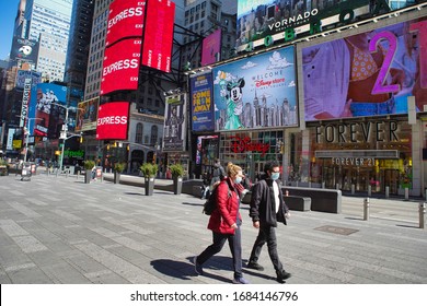 New York, NY / USA - March 26, 2020 - Pedestrians wearing masks walk through a nearly empty Times Square as the corona virus (COVID-19) spreads rapidly throughout New York City and the United States.