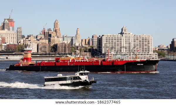 New York, NY, USA - May 1, 2013: Commuter\
boat, forefront, and RTC 82 barge in the East River, Brooklyn\
Heights waterfront in the\
background