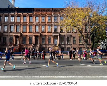 New York, NY USA - November 7, 2021 - Runners pass in front of a row of brownstones near Marcus Garvey Park in Harlem during the 2021 TCS New York City Marathon in New York on November 7, 2021