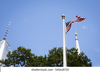 NEW YORK - SEPT 11 2016: Low Angle View Of The American Flag Waving In The Wind Seen Between The Antenna On Top Of The Freedom Tower And Steeple Of St Pauls Chapel In Lower Manhattan.