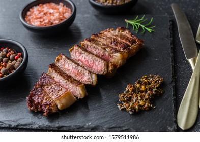 New york strip loin beef steak meat with chimichurri sauce against black stone background