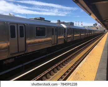 New York Subway Train Passing Through An Overground Metro Station In Queens, New York. Yellow Paint On Very Dirty Subway Platform. Blue Sky And A Few Clouds. Outdoor Subway Station In NYC.