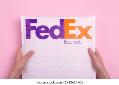 New York, USA - 10 February 2021: Delivery of parcels and cargo by FedEx Express. Hands delivering an order against a pink background.