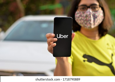 New York, USA, 2020. Girl wearing mask showing Uber app on her mobile phone screen while standing in front of her fleet of cars. Its an aggregator service for booking taxi cabs ride. Concept On the go