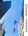 New York, USA - 4 September 2014: View looking up at a blue sky above 5th Avenue in Manhattan with flags of the United States and the spires of St Patricks Cathedral clearly seen.