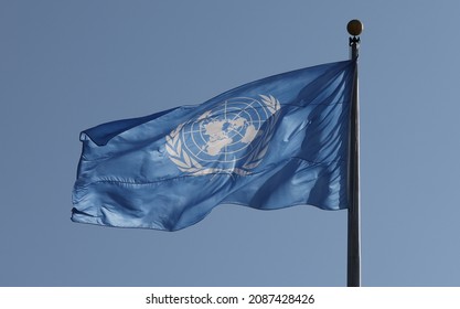 New York, USA - December 1, 2021: Iconic UN blue flag with United Nations emblem flying high at UN Headquarters in NYC. UN blue helmets protecting peace in a peacekeeping mission concept.