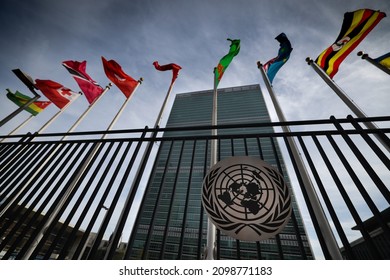 New York, USA - December 1, 2021: UN Emblem, Logo At United Nations Secretariat Building In Focus With Blurred UN Members National Flags Shot At Wide Angle Flying On Background In UN Headquarters