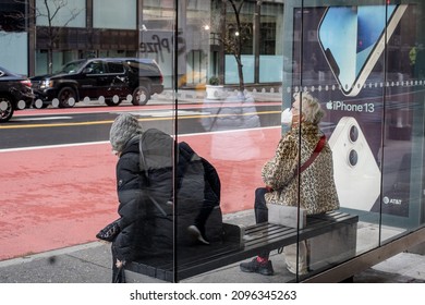 NEW YORK, NEW YORK, USA - DECEMBER 22, 2021: Two Women Sit At Bus Shelter Wearing Face Mask During COVID-19. Pandemic Omicron Wave. 