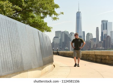 New York, USA - June 09, 2018: Man Near The American Immigrant Wall Of Honor Is Located At The Ellis Island National Museum Overlooks The Lower Manhattan Skyline.