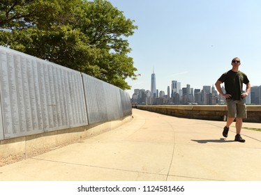 New York, USA - June 09, 2018: Man Near The American Immigrant Wall Of Honor Is Located At The Ellis Island National Museum Overlooks The Lower Manhattan Skyline.