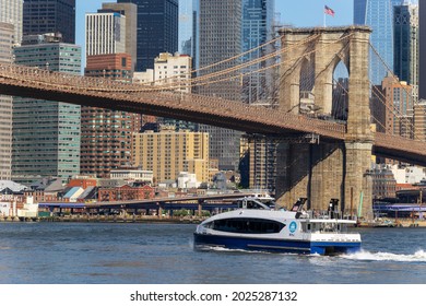 NEW YORK, USA – JUNE 18: NYC Ferry runs on East River at front of the Brooklyn Bridge and Lower Manhattan skyscraper from beach of Brooklyn Bridge Park on June 18, 2021 in Brooklyn New York City.