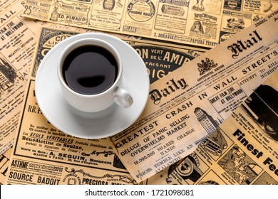 New York, USA - May 01, 2020. A Cup Of Fresh Strong Coffee On A White Saucer Stands Against The Background Of Old Newspapers. Vintage Background From Old Newspapers. Newspaper News The Great Crash 