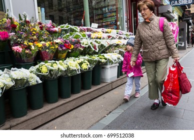 NEW YORK, USA - May 05, 2016: Manhattan street scene. Elderly woman with a child walking past a flowers shop. New Yorkers in Manhattan in a hurry about their business.