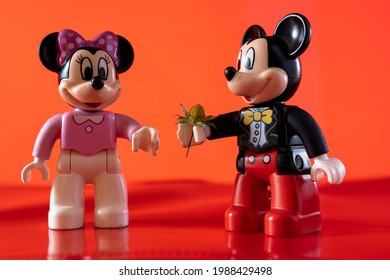 New York, USA - May 25, 2021: A close up shot of a miniature famous Disney character Mickey Mouse Disney character handing over a flower to Minnie Mouse against a red background.