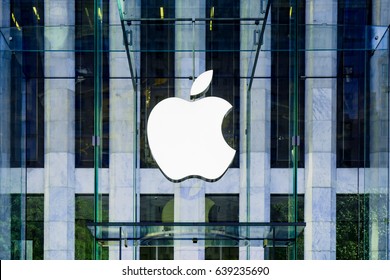 NEW YORK, USA - SEPTEMBER 14, 2016: Apple Store logo hung in the glass cube entrance to the famous Apple Store on Fifth Avenue New York with tourists and shoppers outside, woman takes a photo.