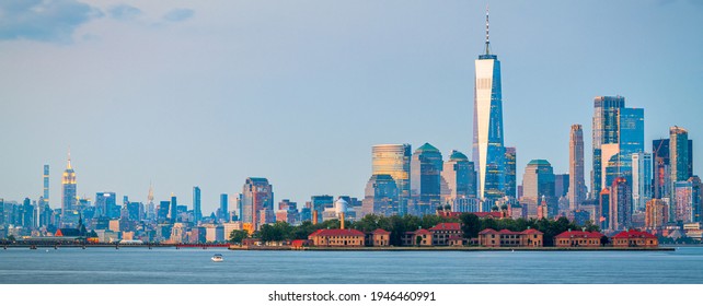 New York, New York, USA skyline from the harbor with Ellis Island at dusk.
