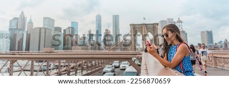 New York woman using phone app walking on Brooklyn Bridge by Manhattan city skyline. Young female professional multicultural lady, New York City, USA. Panoramic banner.