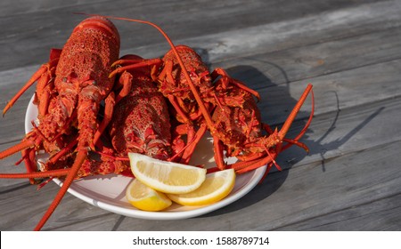 New Zealand Crayfish/rock Lobster On White Plate With Lemon Wedges And Wine Glasses Behind. New Zealand Crayfish Are A Luxury Food Which Is Often Exported To Asia.