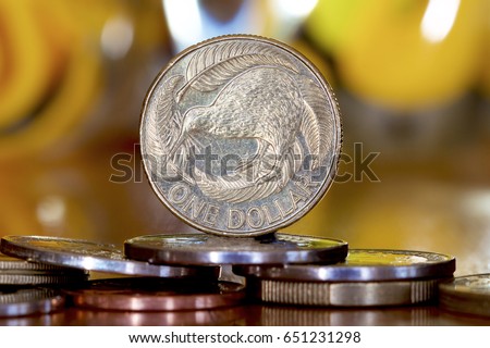 A New Zealand dollar sitting on a pile of coins against a colourful background.
