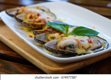 New Zealand mussels baked with cheese on a white plate placed on wooden table at coffee shop.