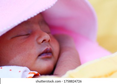 A Newborn Asian Baby Wrapped In Pink Hooded Towel And Sleeping With Eyes Closed.