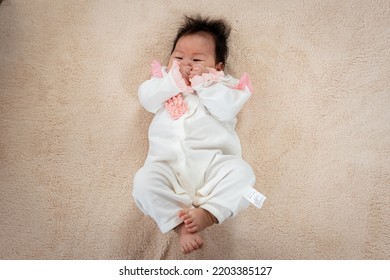 Newborn Asian Girl Lying In White On The Bed Just Waking Up From Sleep. Waiting For Her Mother To Take Care Of Her The Little Boy Rolled Around On The Light Brown Bed.