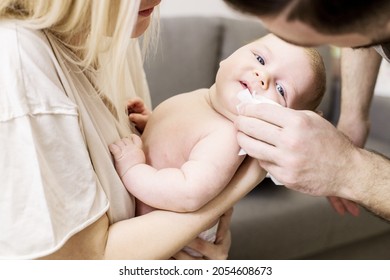 A Newborn Baby In The Arms Of Caring Parents. They Wipe The Baby's Mouth After Feeding And Regurgitation Of Milk. Children, Health Care, Love, Parenting Concept. Authentic Family Moment. Lifestyle.