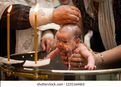 Newborn baby baptism in Holy water. baby holding mother's hands. Infant bathe in water. Baptism in the font. Sacrament of baptism. Child and God. Christening candle Holy water font. The priest baptize