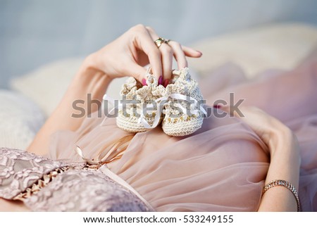 Newborn baby booties in mothers hands. Pregnant woman belly.Close-up image.