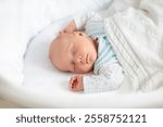 Newborn baby boy in bed. New born child sleeping under a white knitted blanket. Children sleep. Bedding for kids. Infant napping in bed. Healthy little kid shortly after birth. Cable knit textile.