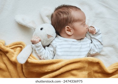 Newborn baby boy in bed sleeping under yellow soft blanket with fluffy rabbit toy comfortable bedding for kids infant child napping in bed - Powered by Shutterstock