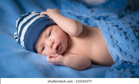 Newborn Baby Boy With Blue Beanie Lies Awake Under Blue Blankets