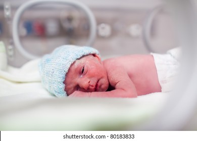 Newborn baby boy covered in vernix in incubator