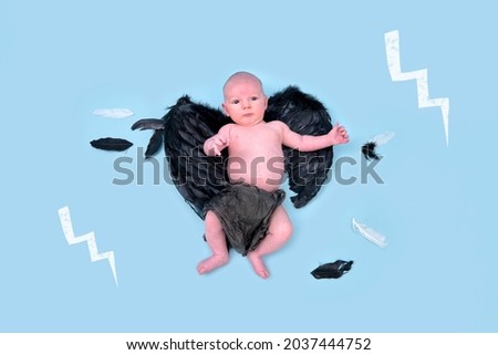 A newborn baby boy with dark demon wings on a blue studio background, copy space. An infant caucasian child in a diaper aged one month
