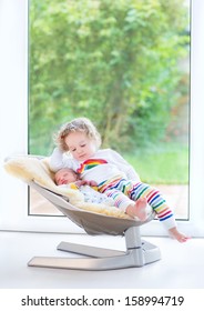 Newborn baby boy and his toddler sister relaxing in a swing next to a big window and door to the garden