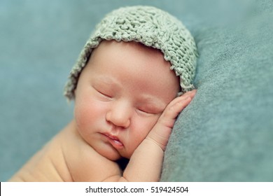 Newborn Baby Boy Sleeping In The Fetal Position On A Blue Background In A Knitted Cap, Face Closeup