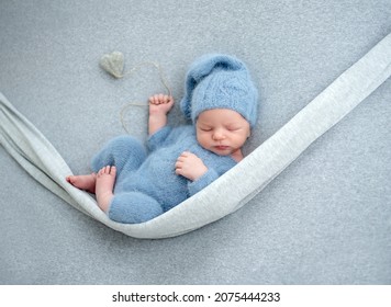 Newborn baby boy sleeping with knitted heart toy during studio photoshoot. Adorable infant child kid sleeping wearing hat and costume - Shutterstock ID 2075444233