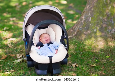 Newborn Baby Boy Sleeping In Modern Car Seat In A Park. New Born Child Traveling By Car. Child Safety On The Road. Safe Way To Travel With Young Kids. Fastened Seat Belts. Trip With An Infant.