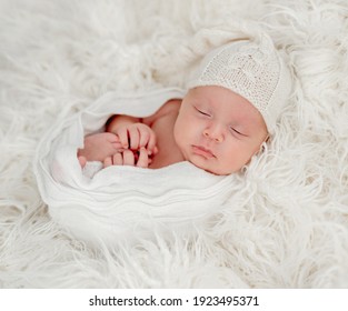 Newborn baby boy sleeping on white fur background wearing rnitted hat. Sweet studio photoshoot of cute infant child