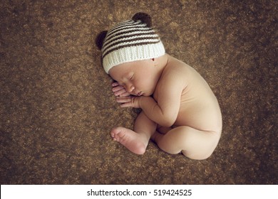 Newborn Baby Boy Sleeping Peacefully In The Fetal Position On A Brown Background 