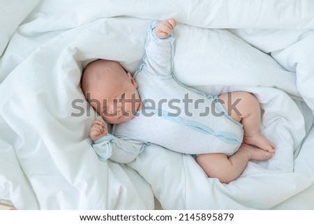 newborn baby boy sleeps seven days in a cot at home on a cotton bed with a toy in his hand, quid on top