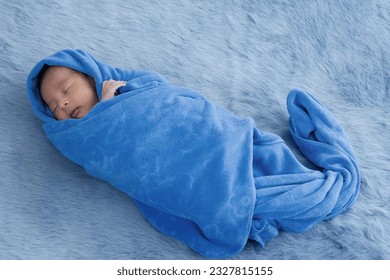 Newborn baby boy wrapped in the blue towel after bathing at home, Newborn baby sleeping in towel wrapped