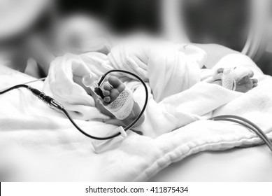 Newborn Baby With Cannula In The Feet On A Hospital Bed