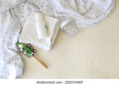 Newborn Baby Care Items Are On The Table. A Muslin Swaddle, A Cute Rattle, Powder And A Baby Bottle With A Pacifier. Place For Text. Nobody. Top View.