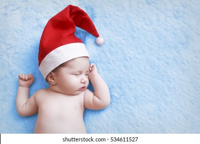 Newborn Baby In A Christmas Cap Sleeps On Blue Background