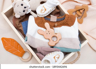 Newborn Baby Clothes And Wooden Toys In A Box On A Light Background. Top View, Flat Lay.