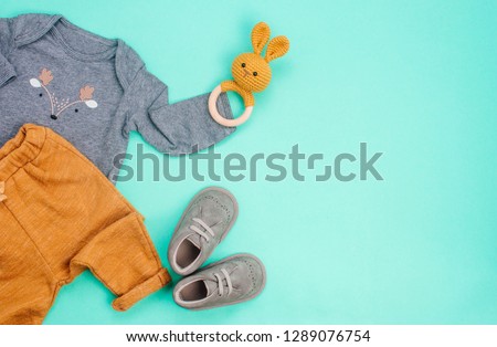Newborn baby clothing and rabbit beanbag on turquoise background with blank space for text. Top view, flat lay.