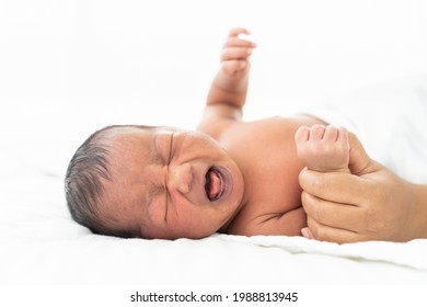 Newborn Baby Crying. Infant Crying. African American Newborn Baby Or Infant Lying On White Bed With Mother’s Hands Takes Care Carefully. Family, Love And New Life Concept